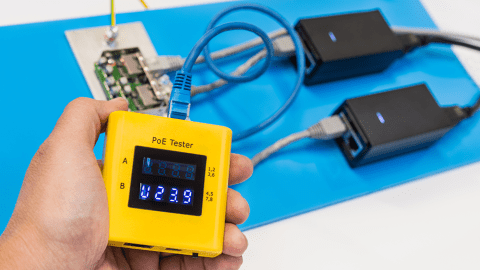 Human palm holding yellow diagnostic digital gauge. Two switched supplies, electric wires and surge protector on blue plastic
